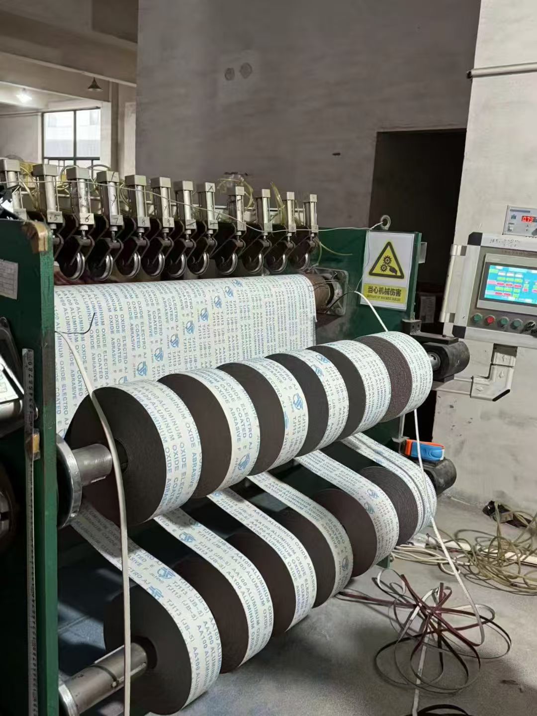 Abrasive paper rolls being slit on factory machinery