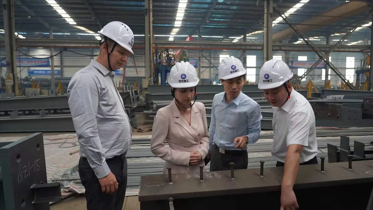 Visitors wearing hard hats discussing a steel component with staff on the factory floor